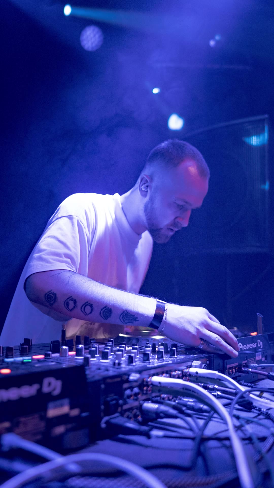 DJ in a white shirt working the mixer in blue haze