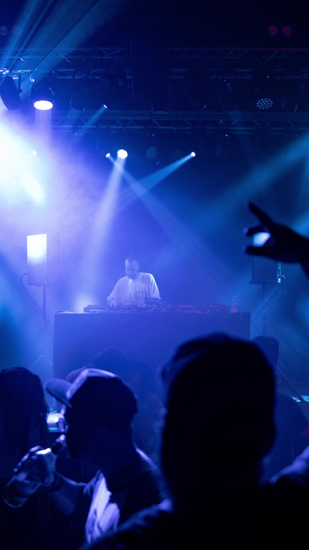 Crowd silhouettes with hands up toward the stage beams