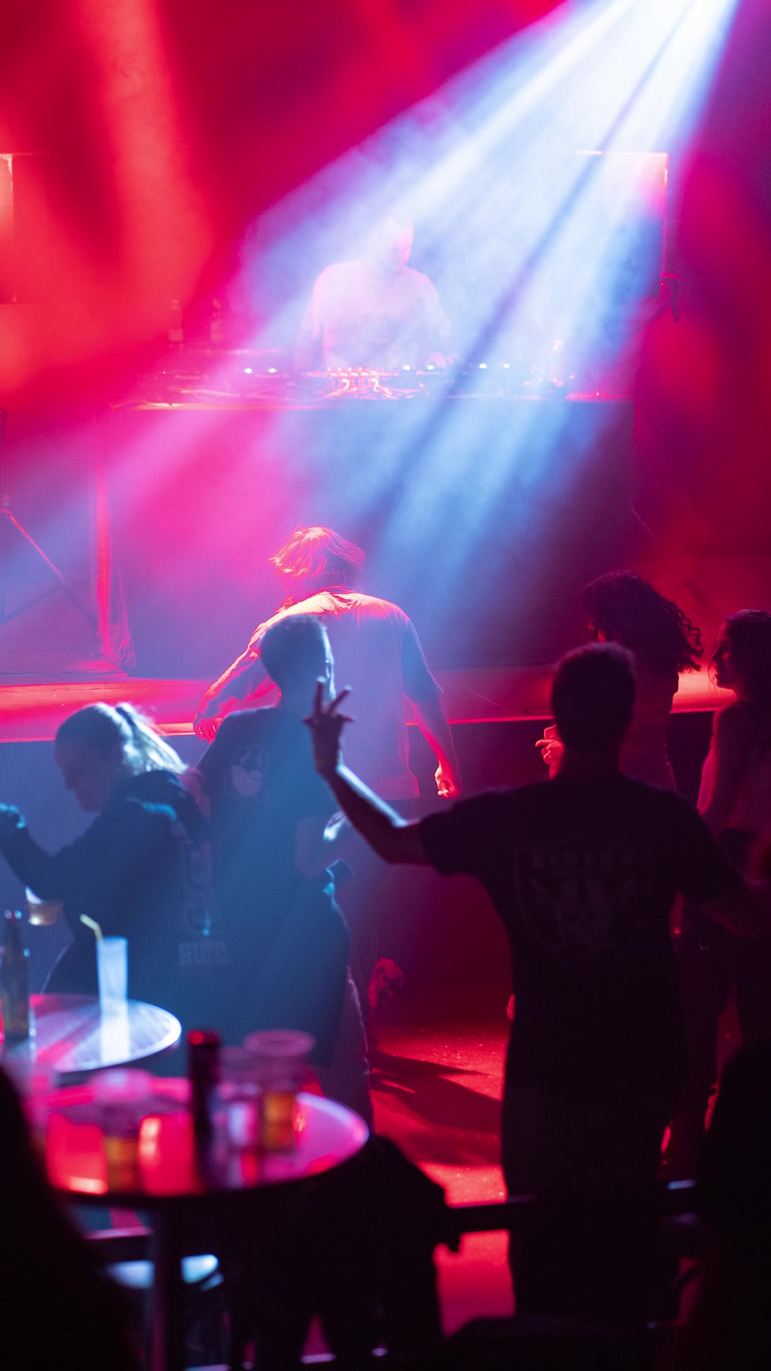 Crowd dancing under red and white stage beams in front of the DJ booth
