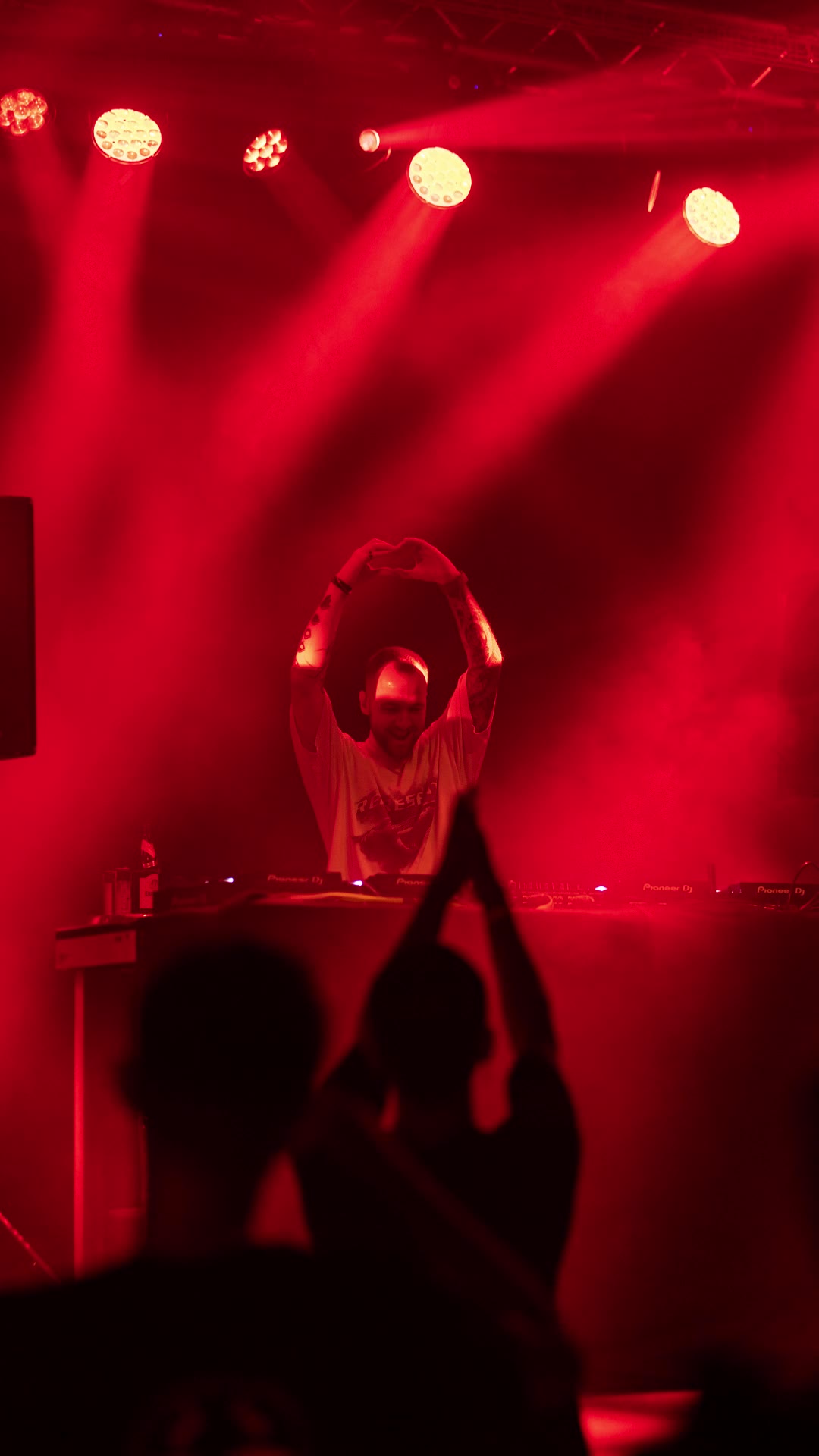 DJ under red stage lights with the crowd clapping in front