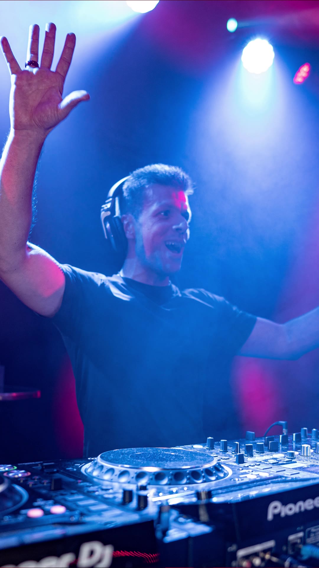 DJ with both arms up behind the decks in blue light