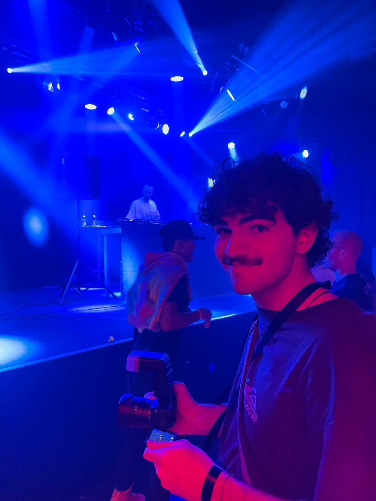 Damiano with camera and flash in front of the DJ booth under blue light